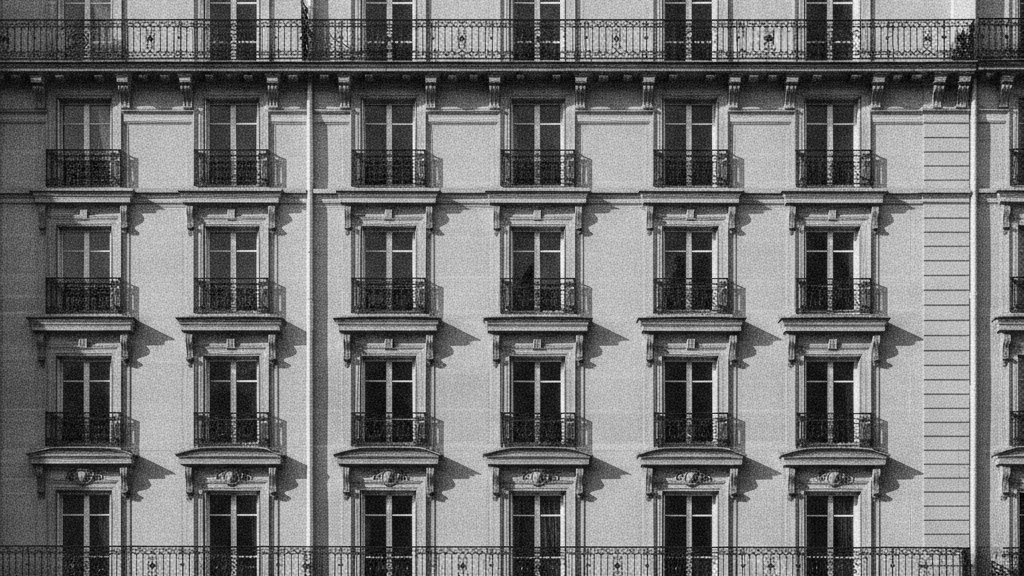 Façade d'immeuble haussmannien à balcons en fer forgé, lumière rasante de fin d'après-midi, périmètre strict de l'IFI immobilier